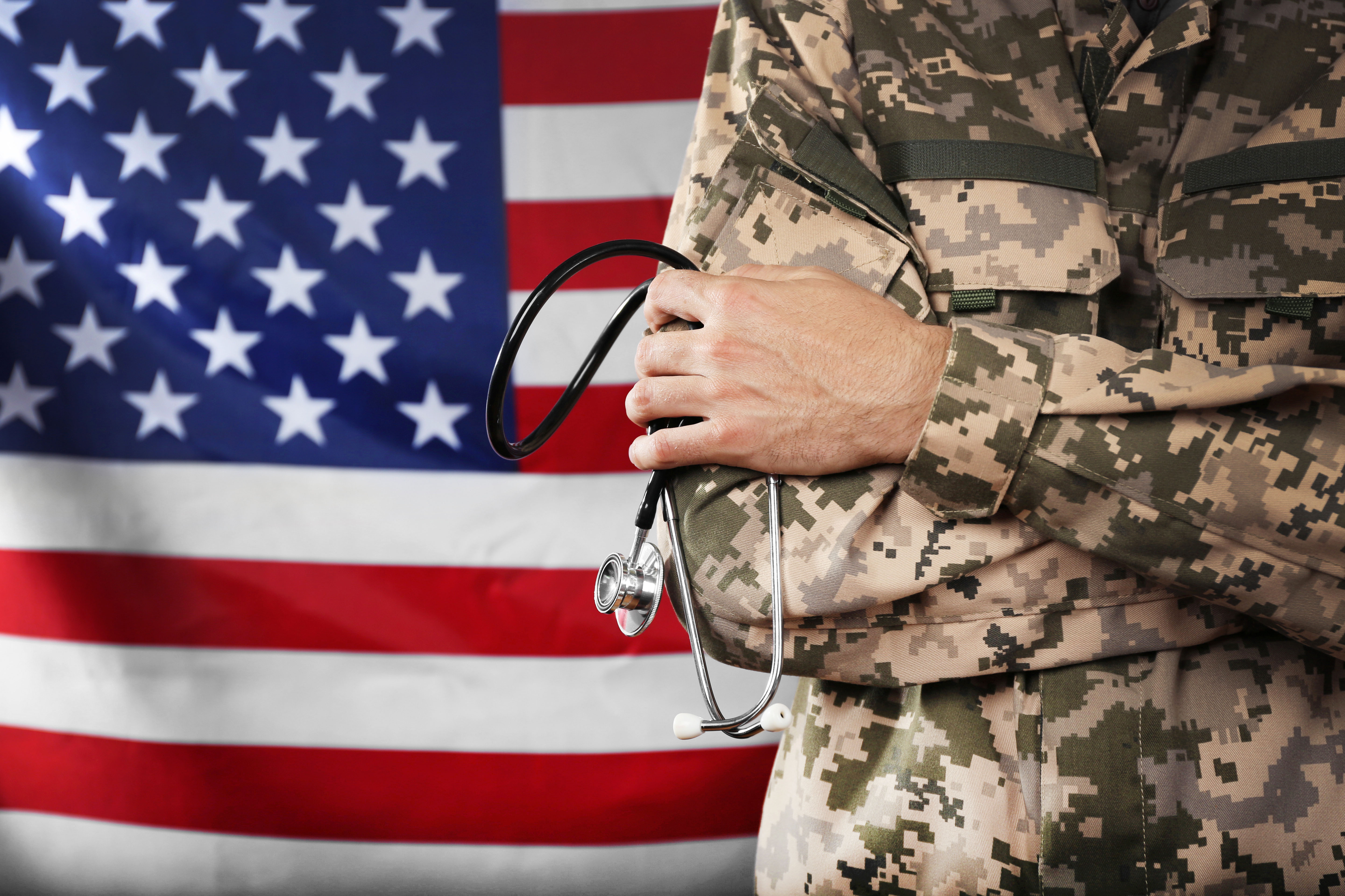 Soldier holds stethoscope in front of United States flag